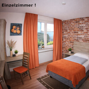 Einzelzimmer im Landhotel Römerkessel mit Einzelbett, Backstein-Akzentwand, orangefarbenen Vorhängen, Sitzgelegenheit und hellem Holzfußboden.